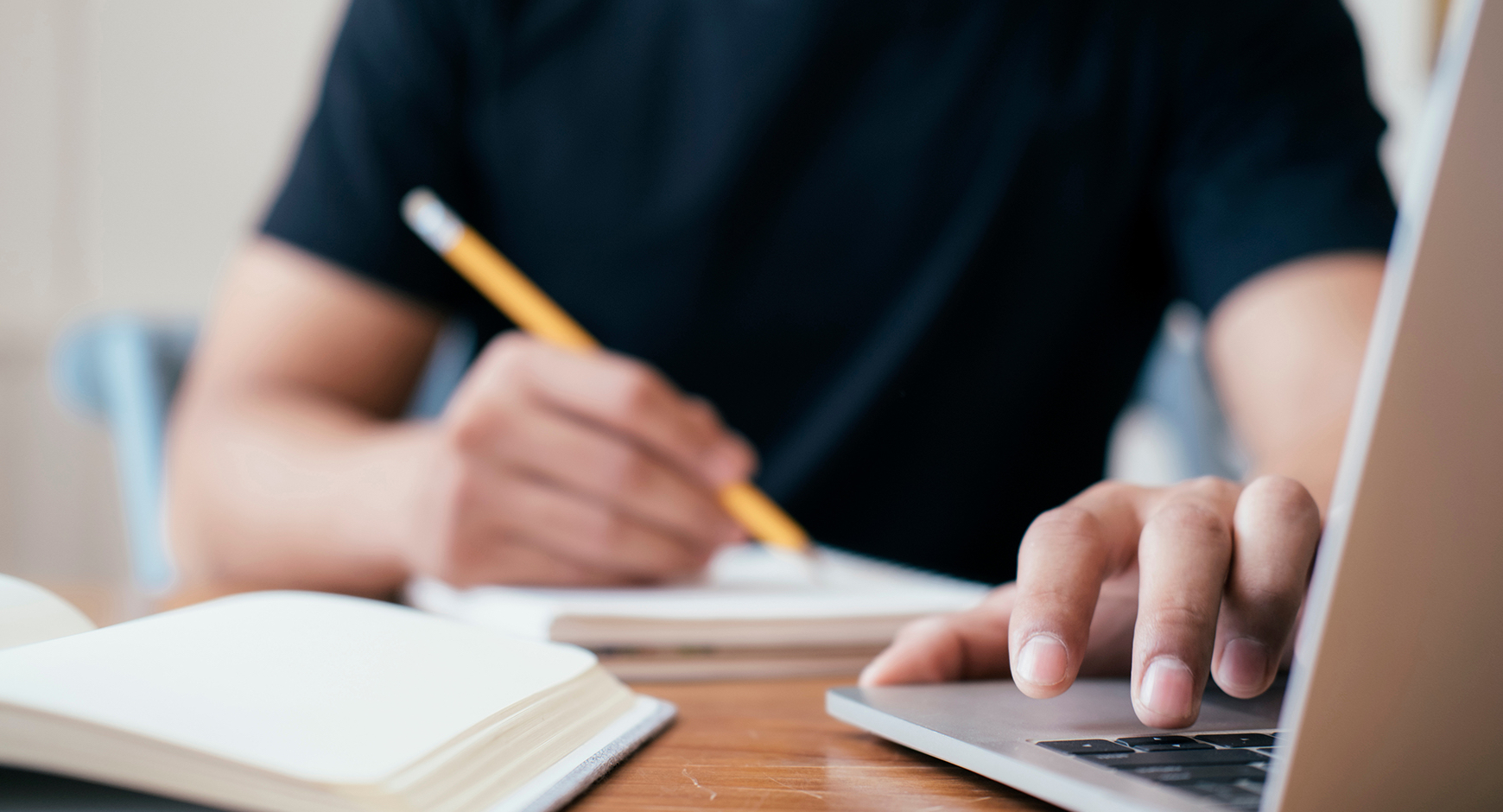 Student taking notes in journal with their laptop open