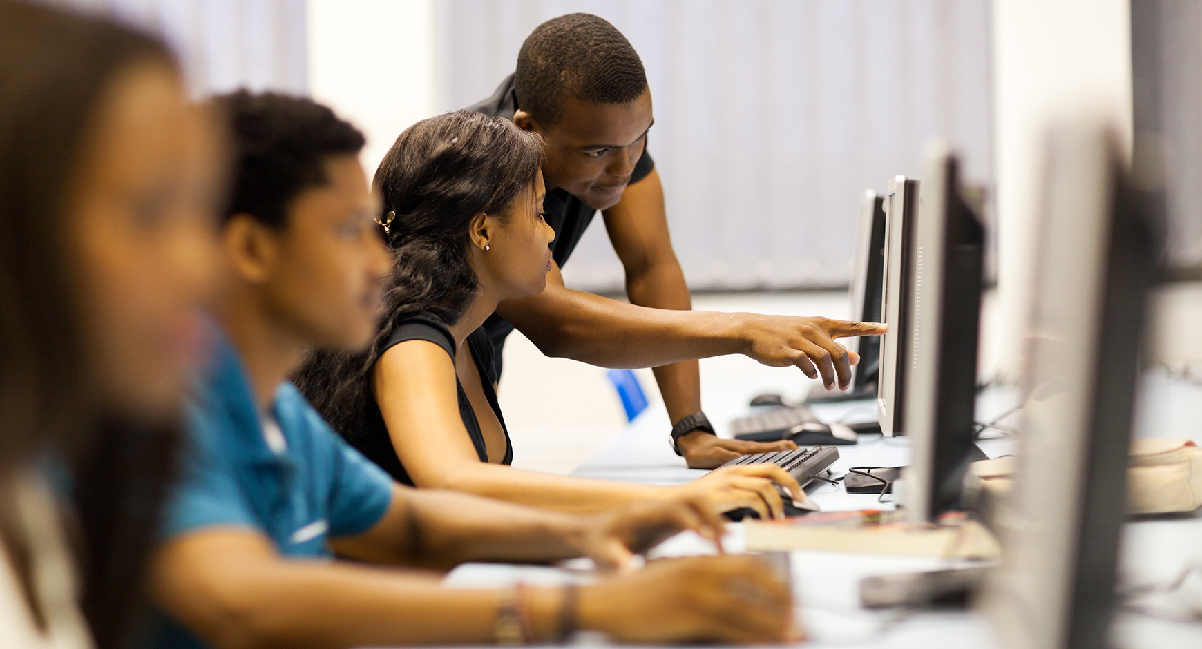 Black male teacher showing students how to perform an operation on a desktop computer